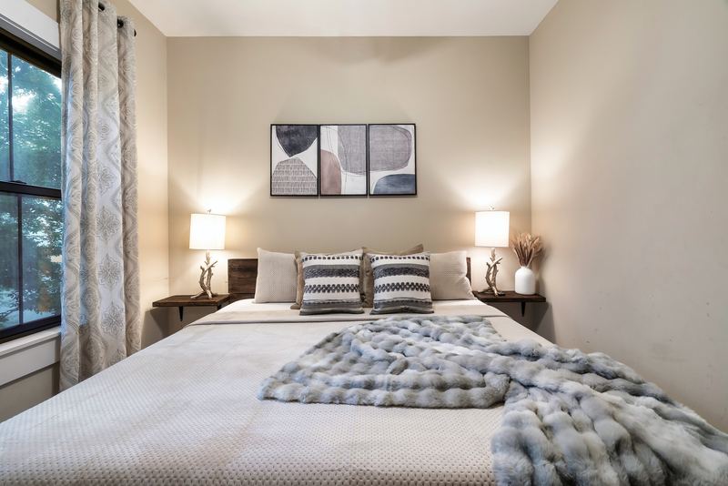 Main-level king bedroom with two bedside lamps, a gray throw and a window