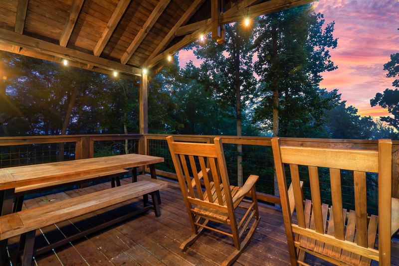 Covered upper deck with a long picnic table and wooden rocking chairs at sunset